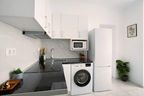 Una cucina compatta con lavatrice, forno a microonde e frigorifero.
