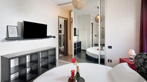 A modern hotel room with a large bed, a TV on a shelf, a mirror, and a bedside table with a lamp.