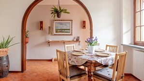 Un coin repas avec une table dressée pour quatre personnes, des chaises en bois, une plante suspendue, un tableau encadré au mur et une fenêtre donnant sur un beau paysage.