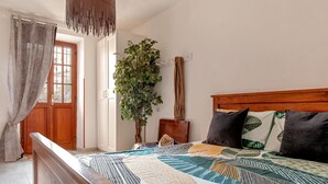 Une chambre à coucher avec un lit en bois, une grande fenêtre avec des rideaux, une plante en pot et une tête de lit en bois.