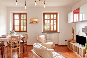 Un comedor con una mesa dispuesta para dos, un sofá y un televisor sobre un mueble.