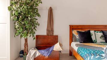 Une chambre avec une tête de lit en bois, un lit recouvert d’une literie à motifs, une plante suspendue et une petite commode en bois.