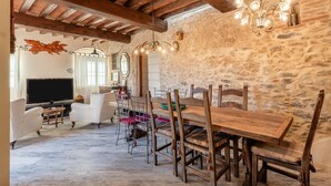 A rustic interior with exposed stone walls, wooden beams, a dining area with a long wooden table and chairs, a television, and a chandelier. - Holiday Home 'La Capanna Di Arturo Ground Floor' with Mountain View, Wi-Fi and Air Conditioning (Capannori)