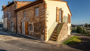Un bâtiment en pierre avec un escalier menant à une porte, le tout baigné d’un ciel clair et entouré de verdure.
