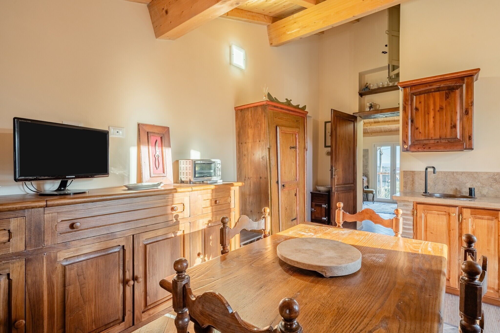 Un tavolo da pranzo in legno con sedie, una televisione, un forno a microonde e pensili in legno in una zona cucina.