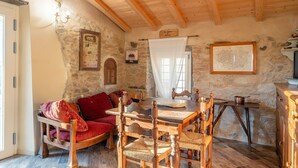 Une pièce rustique avec un mur en pierre, des poutres en bois au plafond, une table à manger avec des chaises, un canapé rouge et un petit coin cuisine.