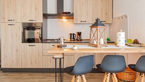 Eine moderne Küche mit Holzausstattung, einem Einbauofen, einer Kaffeemaschine und einem Essbereich mit Stühlen und einem Tisch.