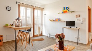 Ein modernes Wohnzimmer mit Essbereich, Fernseher und einem großen Fenster mit Vorhängen.
