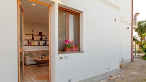 Ein Zimmer mit einer Couch, einem kleinen Tisch, einem Fenster mit Blumenkasten und einer Tür zu einem anderen Raum.