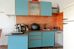 Una cocina compacta con armarios color turquesa, microondas, cafetera y lavavajillas.