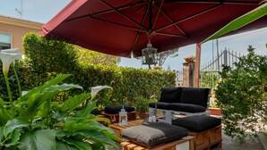 Ein Patio mit rotem Sonnenschirm, Holzmöbeln und Kübelpflanzen.