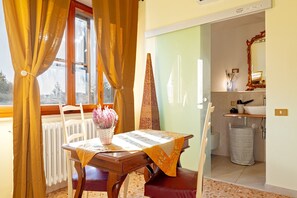 A dining area with a table set for two, a potted plant, and a window with curtains.