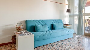 Ein Zimmer mit einem blauen Sofa, einem kleinen weißen Beistelltisch, einer Glasvase mit Steinen und einem Fliesenboden.