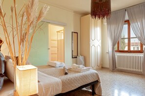 Un dormitorio con cama, lámpara de noche, espejo, radiador y ventana con cortinas.