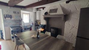 Una cocina con pared de piedra, vigas de madera, una mesa de comedor, sillas, estufa y una ventana.