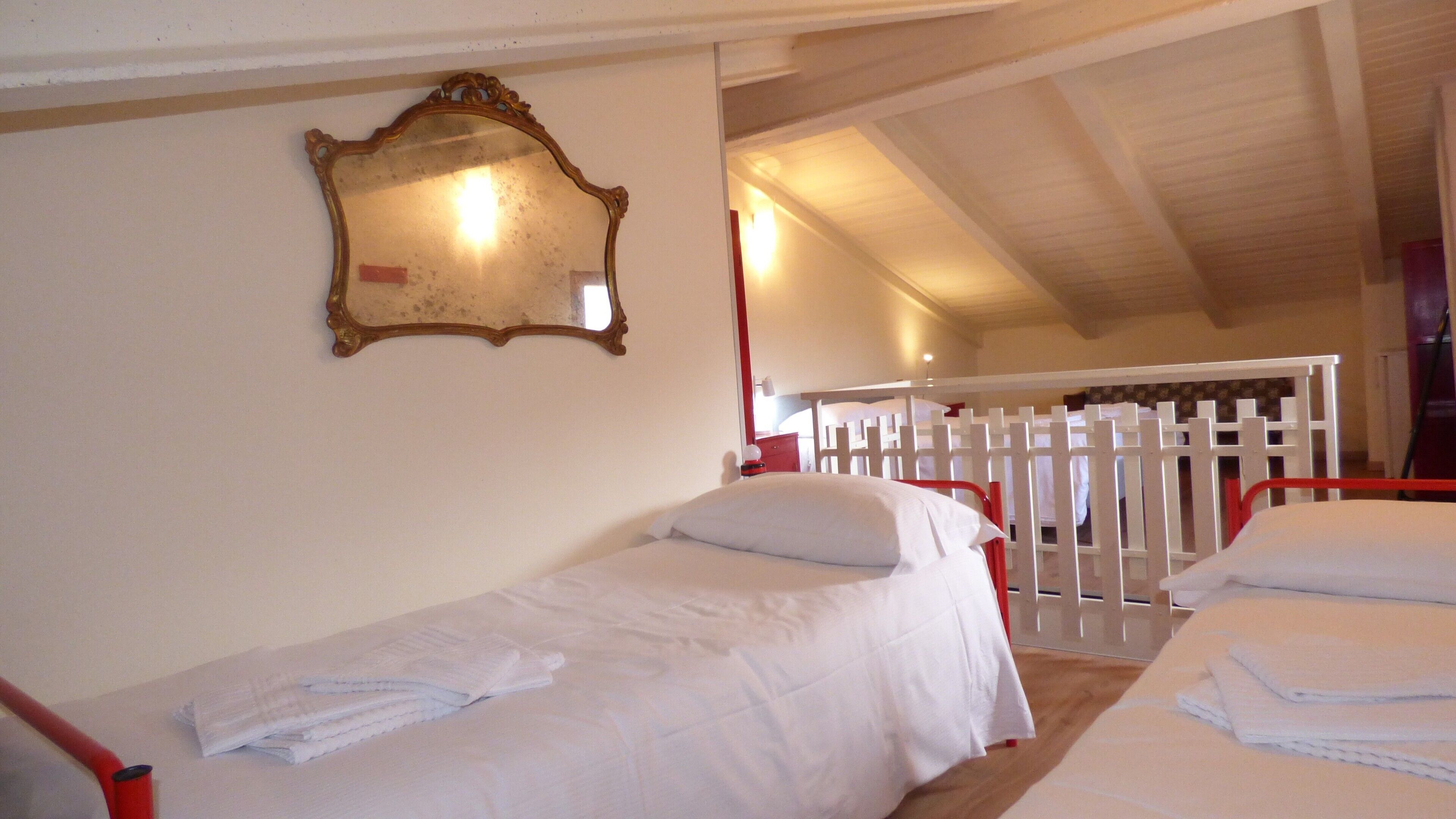 A room with two beds, a wooden ceiling, a white railing, and a mirror on the wall.