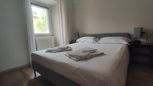 A neatly made bed with pillows and folded towels, a bedside table with a lamp, and a window with curtains. - Holiday Home 'Gnazzano Home 1' with Mountain View, Wi-Fi and Air Conditioning (Loiano)