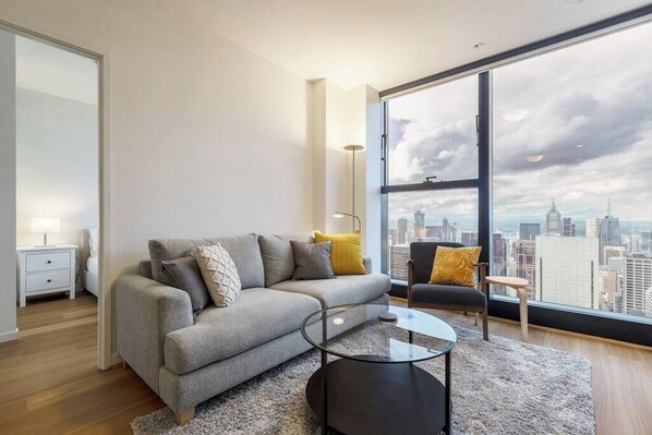 A modern living room with a sofa, a glass coffee table, and a view of a cityscape through large windows.