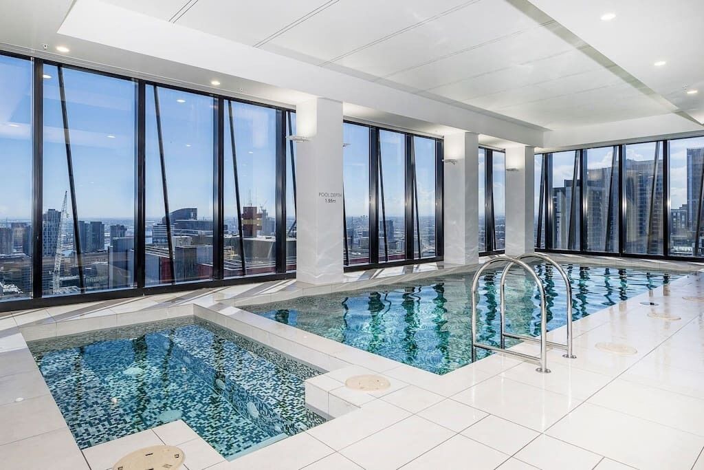 A modern indoor pool with clear city views, large windows, and a tiled floor.