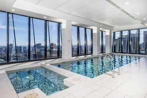 A modern indoor pool with clear city views, large windows, and a tiled floor.