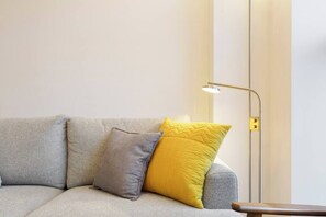 A sofa with two pillows, a floor lamp, and a wooden side table.