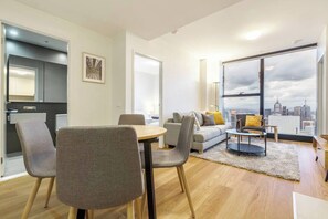 Uma sala de estar moderna com um sofá, cadeiras, uma mesa de jantar e vista para um horizonte urbano através de grandes janelas.