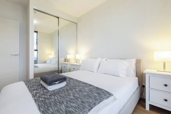 A hotel room with a bed, a nightstand with a lamp, a mirror, and a door leading to another room.