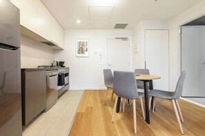 A modern kitchen with stainless steel appliances, a dining area with grey chairs, and a wooden floor.