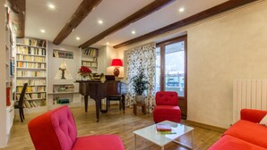 Un salon avec un piano, des fauteuils rouges, une table basse et des étagères remplies de livres.