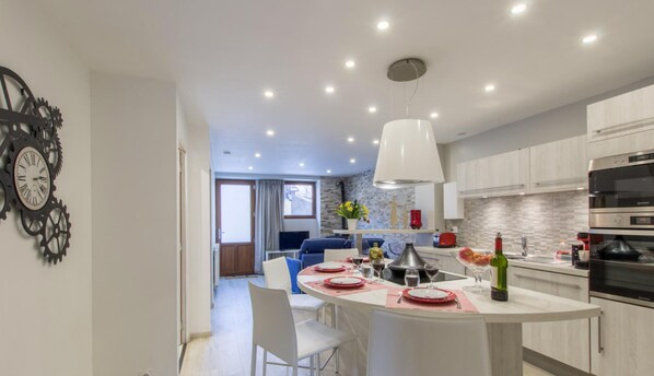 Una cocina moderna con una isla central, electrodomésticos de acero inoxidable y un comedor con una mesa dispuesta para dos.