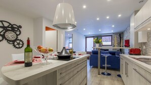 Une cuisine moderne dotée d’un îlot central, d’un coin repas avec un canapé bleu et d’un comptoir de cuisine sur lequel se trouvent une bouteille de vin et des fruits.