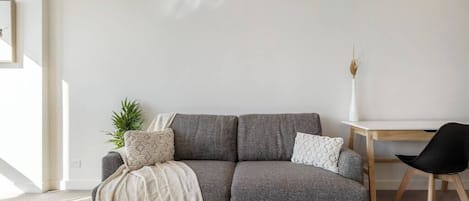 A modern living room with a grey sofa, a wooden coffee table, a white desk, and a black chair.