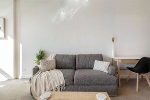 A modern living room with a grey sofa, a wooden coffee table, a white desk, and a black chair.