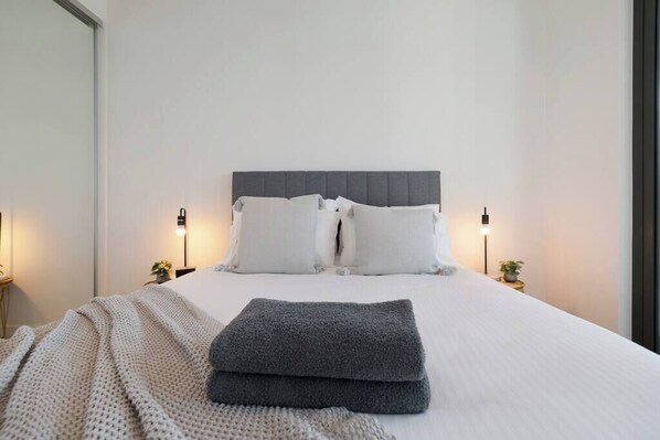 A neatly made bed with pillows, a grey blanket, and bedside lamps.
