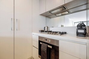 A modern kitchen with white cabinetry, a stainless steel stove, and a coffee maker.