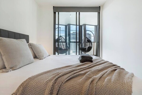 A hotel room with a bed, a large window, and a view of the city.