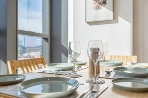 A dining table set with plates, cutlery, and wine glasses, with chairs around it.