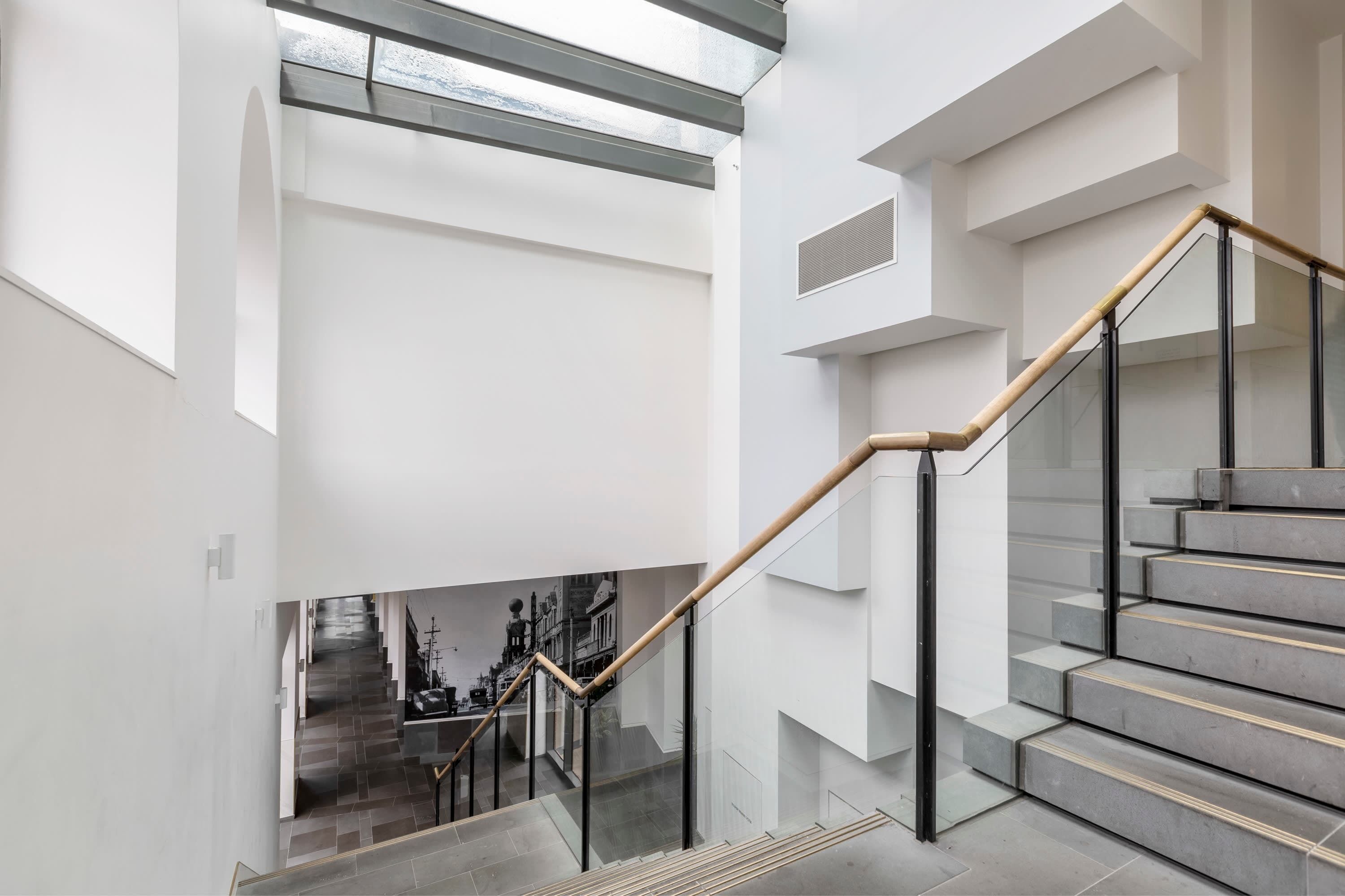 Een modern interieur met een trap, glazen balustrades en uitzicht op een stadsgezicht door een open ruimte.