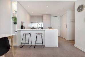 A modern kitchen with white cabinetry, a central island with stools, and a clock on the wall.