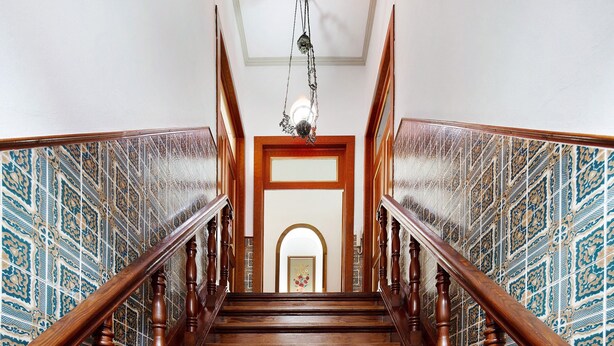 Una escalera de madera con un diseño en la pared a cada lado, que conduce a una puerta con un cuadro enmarcado.