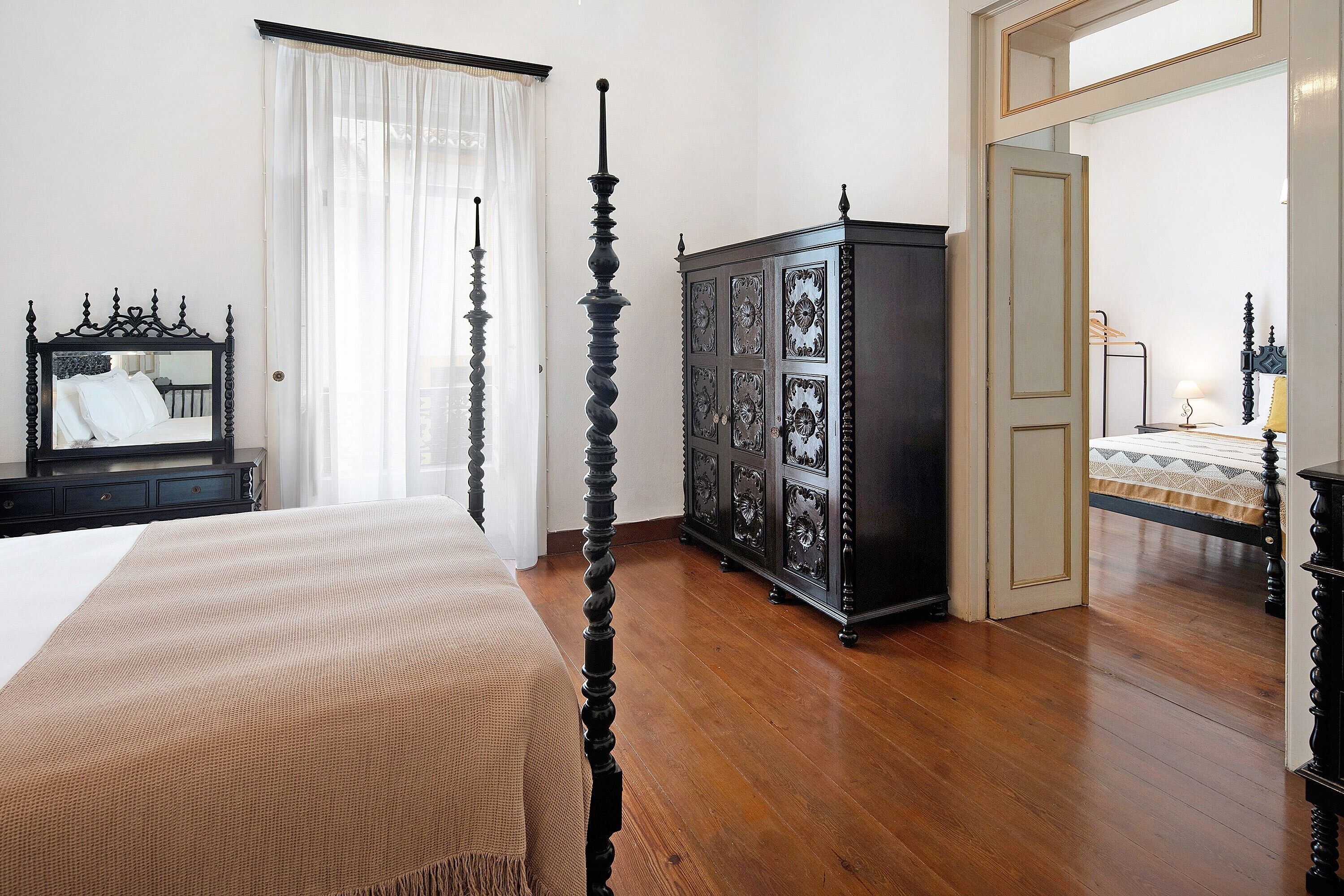 A bedroom with a four-poster bed, a dark wooden cabinet, and a mirror on the wall.
