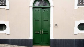 Una puerta verde doble con un aldabón de latón, una placa con un nombre y un pequeño ventanal encima.