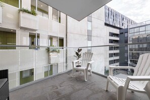 A balcony with two white chairs, a potted plant, and a glass railing.