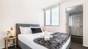 Une chambre d’hôtel moderne avec un grand lit, une table de chevet avec une lampe, une fenêtre et un espace douche.