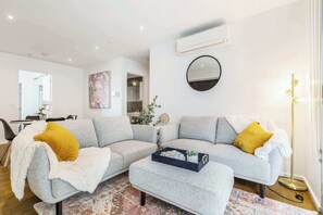 A modern living room with a grey sofa, a small ottoman, a round mirror, and a floor lamp.