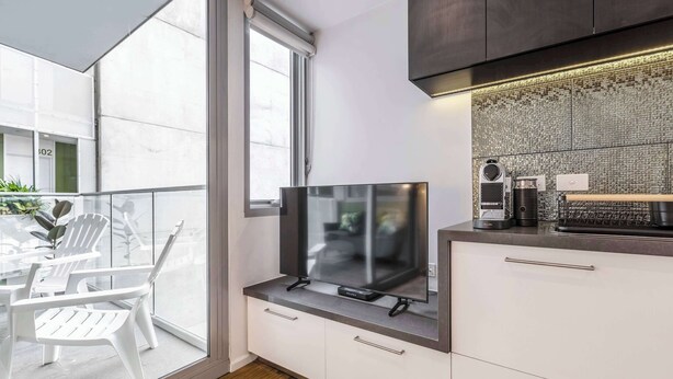 Une cuisine moderne dotée d’une grande fenêtre, d’un téléviseur à écran plat et d’un petit coin repas avec des chaises blanches.