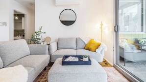 Un salon moderne avec un canapé gris, un miroir rond et une petite table agrémentée d’objets décoratifs.