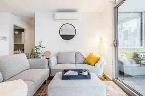 A modern living room with a grey sofa, a round mirror, and a small table with decorative items.