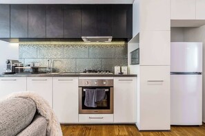 A modern kitchen with dark cabinets, a tiled backsplash, stainless steel appliances, and a white refrigerator.