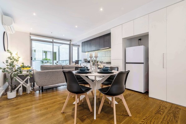 A modern kitchen with a dining area, white cabinets, and a large window.